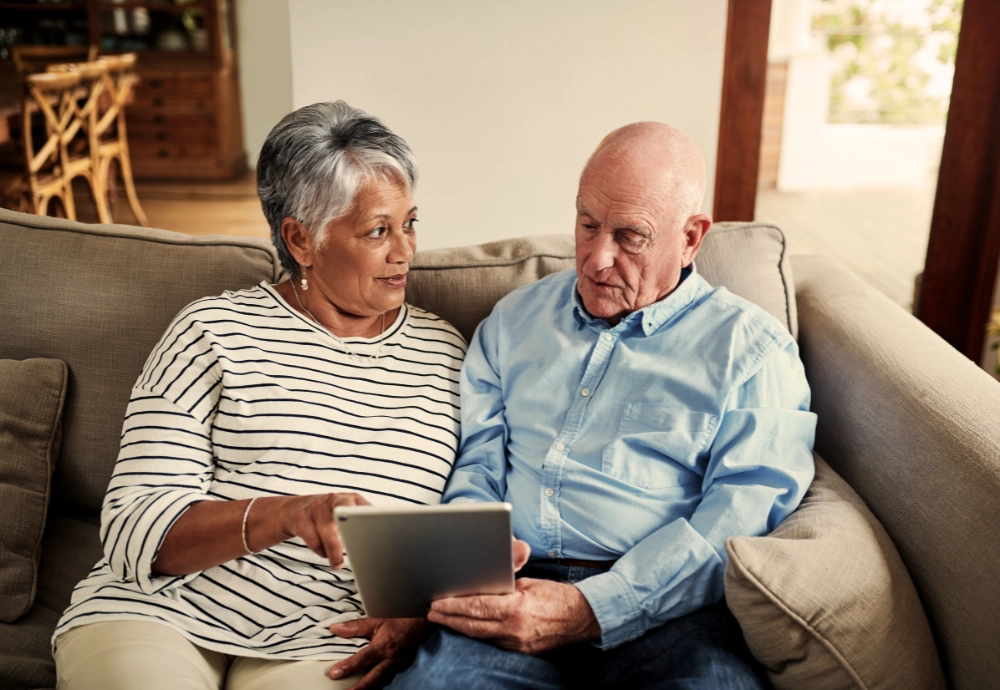 A woman and man look at a tablet while sitting on a couch.